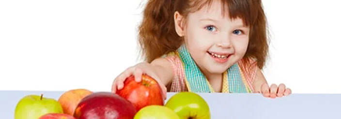 Niña cogiendo una manzana y mirando a cámara