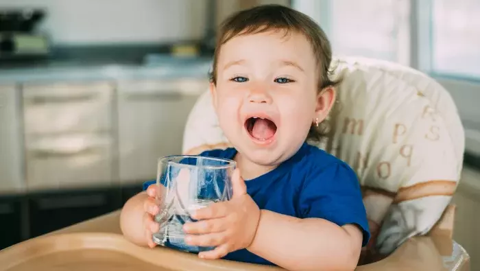  Niña en la trona bebiendo un vaso de agua