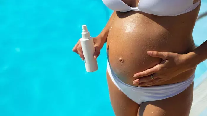 Mujer embarazada poniéndose crema protectora para tomar el sol en la piscina